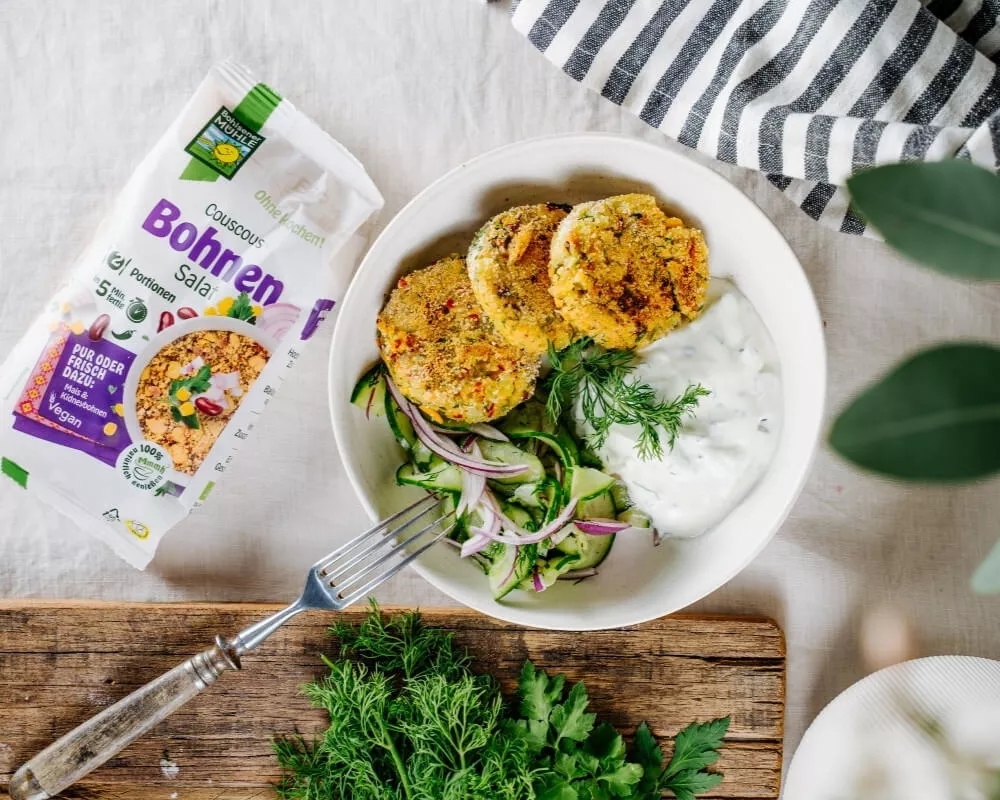 Bohlsener Mühle Bio-Bohnen-Couscous-Salat mit veganen Patties, Gurke, roten Zwiebeln und Dill-Joghurt-Sauce.