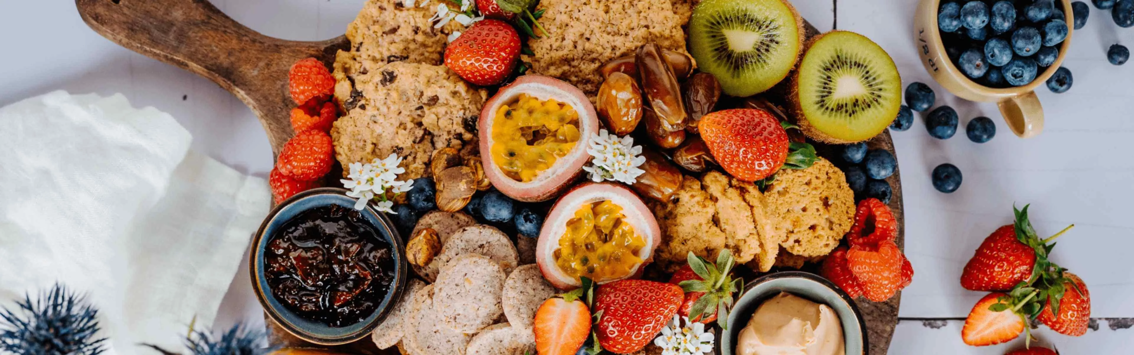 Bohlsener Mühle Crunchy Cookies mit frischen Früchten und Dips auf einem Holzbrett.