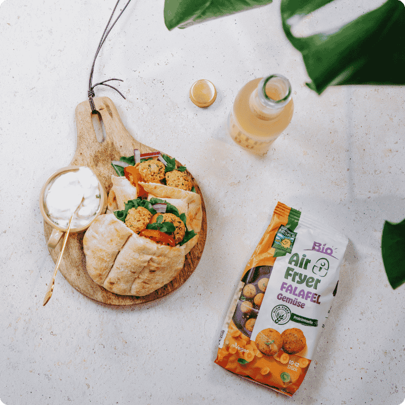 Bohlsener Mühle Air Fryer Falafel Gemüse in einem Fladenbrot mit Dip auf einem Holzbrett serviert.