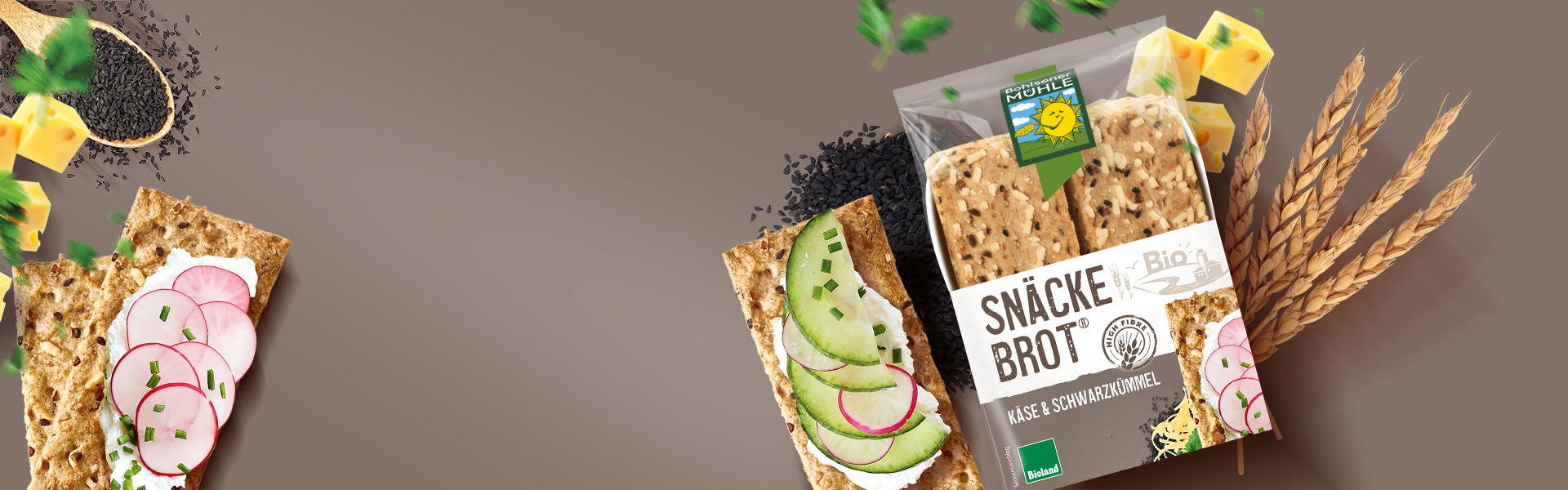 Bohlsener Mühle Snäcke Brot Käse & Schwarzkümmel mit Radieschen, Gurken und Käsewürfeln auf braunem Hintergrund.