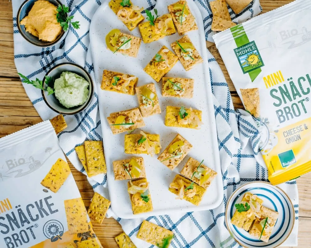 Bohlsener Mühle Bio-Mini-Snackbrot mit Käse und Zwiebeln, serviert mit Dips, zur Förderung einer nachhaltigen Landwirtschaft.