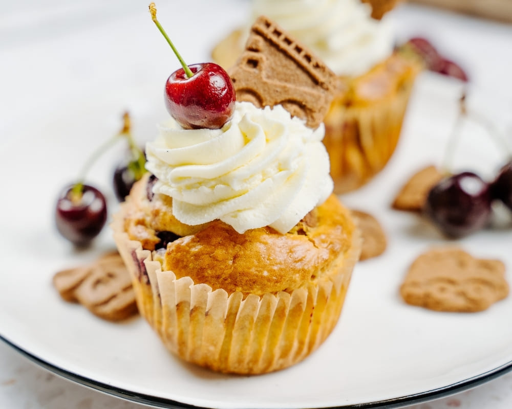 Bohlsener Mühle Crunchy Cookie Muffin mit Sahnehaube, Kirsche und Keks auf einem weißen Teller angerichtet.