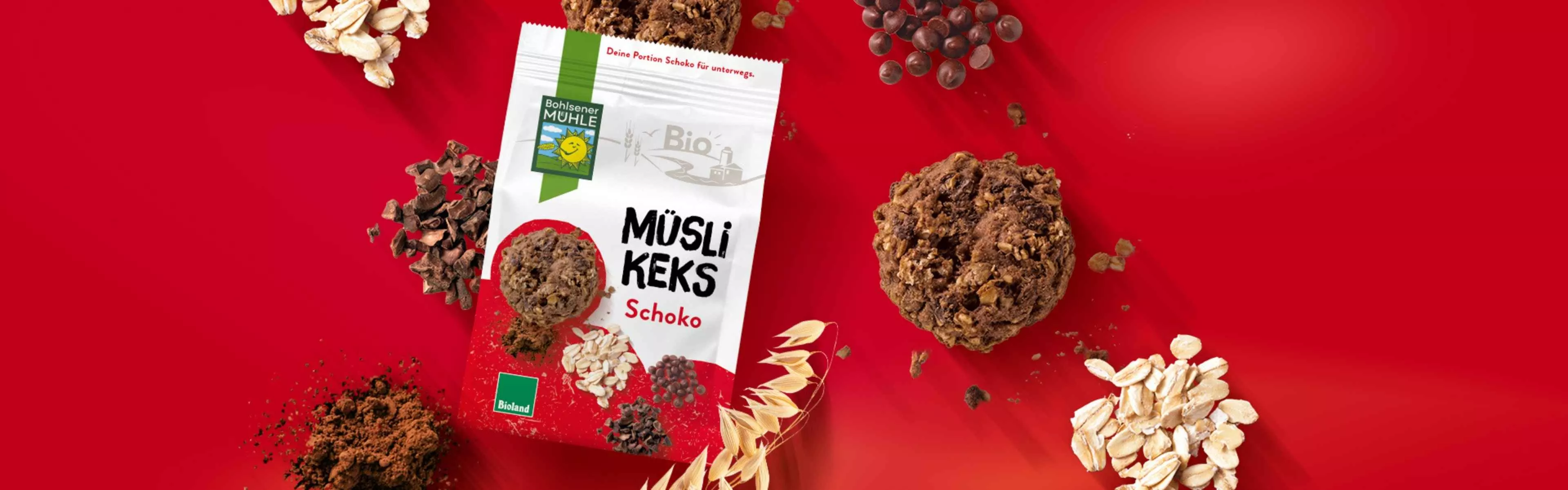 Bohlsener Mühle Müsli Keks Schoko auf rotem Hintergrund mit Schokoladenstückchen und Haferflocken.
