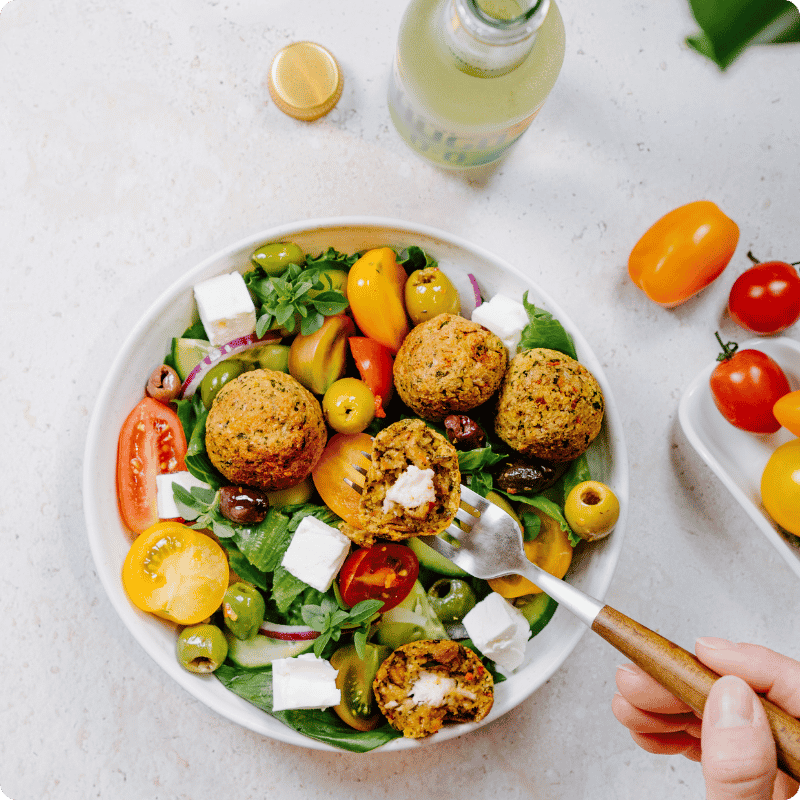 Bohlsener Mühle Knusprige Falafel in einem frischen Salat mit Feta, Tomaten und Oliven auf einem weißen Teller serviert.