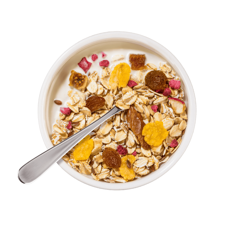 Eine Schale mit Bohlsener Mühle Früchte Crunchy Müsli und Milch sowie ein Löffel auf grünem Hintergrund.