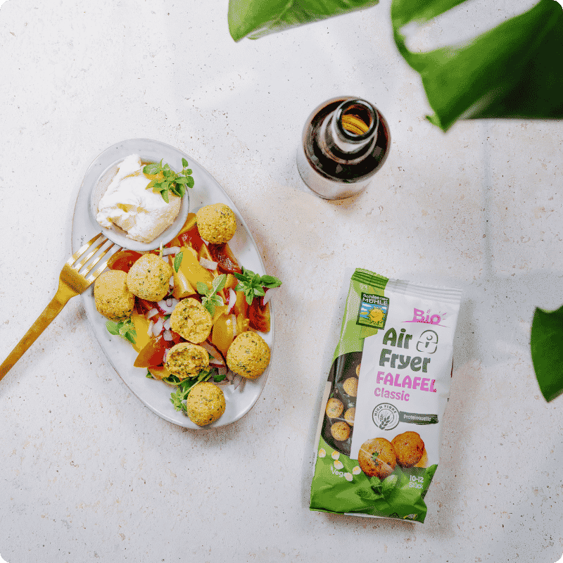 Bohlsener Mühle Air Fryer Falafel Classic neben einem Teller mit Falafelbällchen, Salat und einer kleinen Schale Dip.