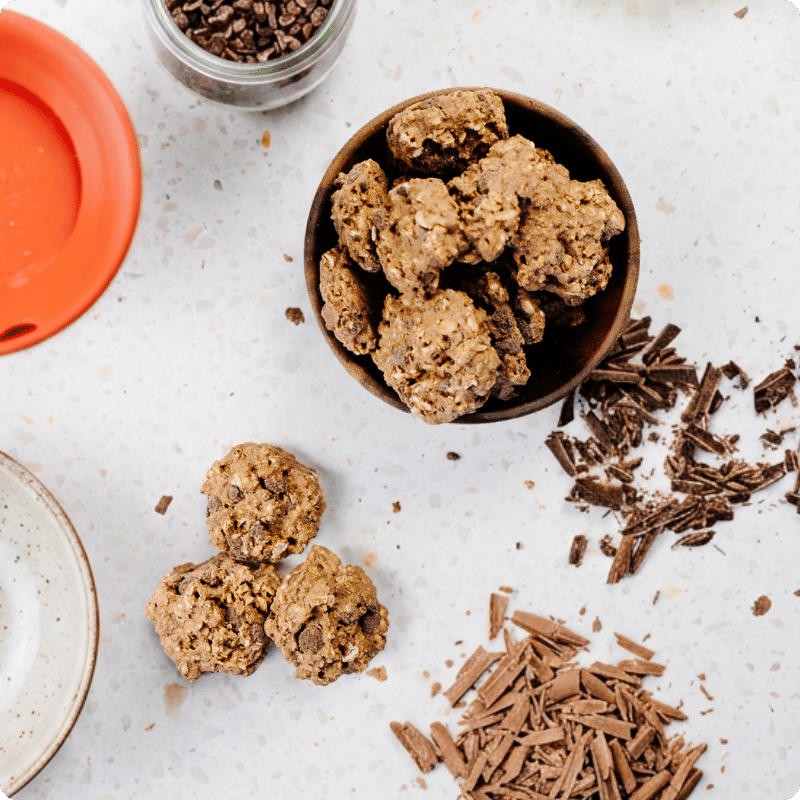 Bohlsener Mühle Crunchy Cookie in einer Holzschale, umgeben von Schokoladenraspeln auf einer hellen Arbeitsplatte.