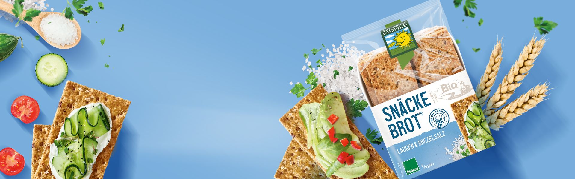 Bohlsener Mühle Snäcke Brot Laugen & Brezelsalz mit Avocado, Gurken und Tomaten auf blauem Hintergrund angerichtet.