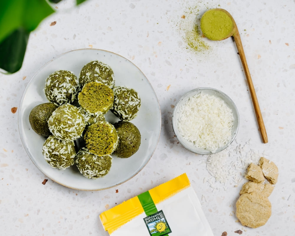Bohlsener Mühle Crunchy Cookie Bällchen mit Kokosraspeln und Matcha-Pulver auf einem Teller.