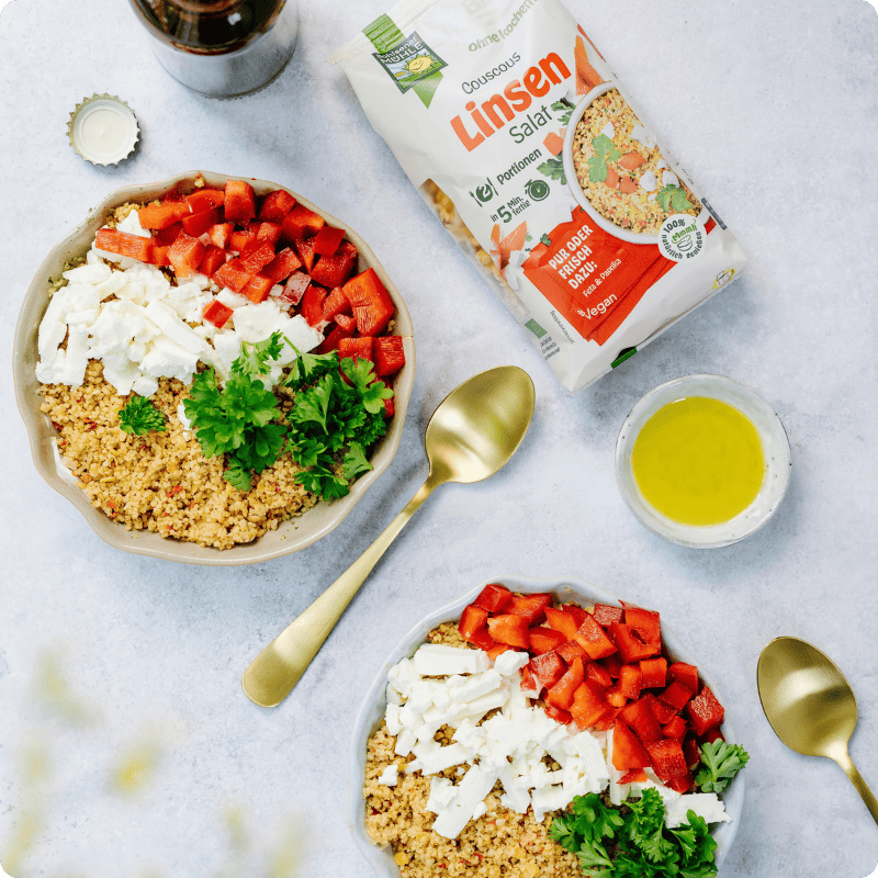 Zwei Schalen mit Bohlsener Mühle Couscous Linsen Salat, garniert mit frischem Paprika, Feta und grüner Petersilie.