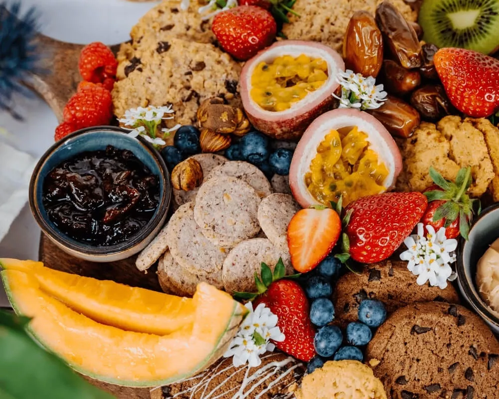 Eine farbenfrohe Platte der Bohlsener Mühle mit Bio-Keksen, Müsli, knusprigen Snacks und schnellen Mahlzeiten. Enthält frische Früchte wie Erdbeeren, Blaubeeren, Passionsfrüchte, Melonen und Datteln.