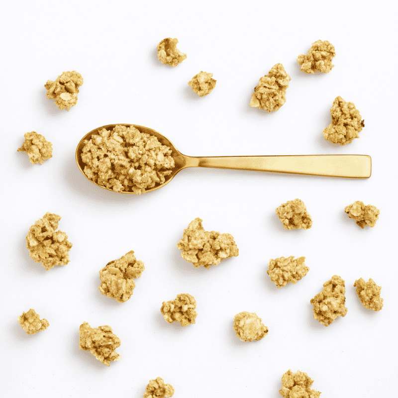 Ein goldener Löffel mit Bohlsener Mühle Cookie Crunchy Müsli umgeben von einzelnen knusprigen Haferflocken-Stücken.