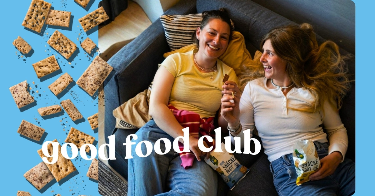 Zwei Frauen essen Bohlsener Mühle Mini Snackebrot auf einem Sofa, umgeben von fliegenden Crunchy Brotstücken.