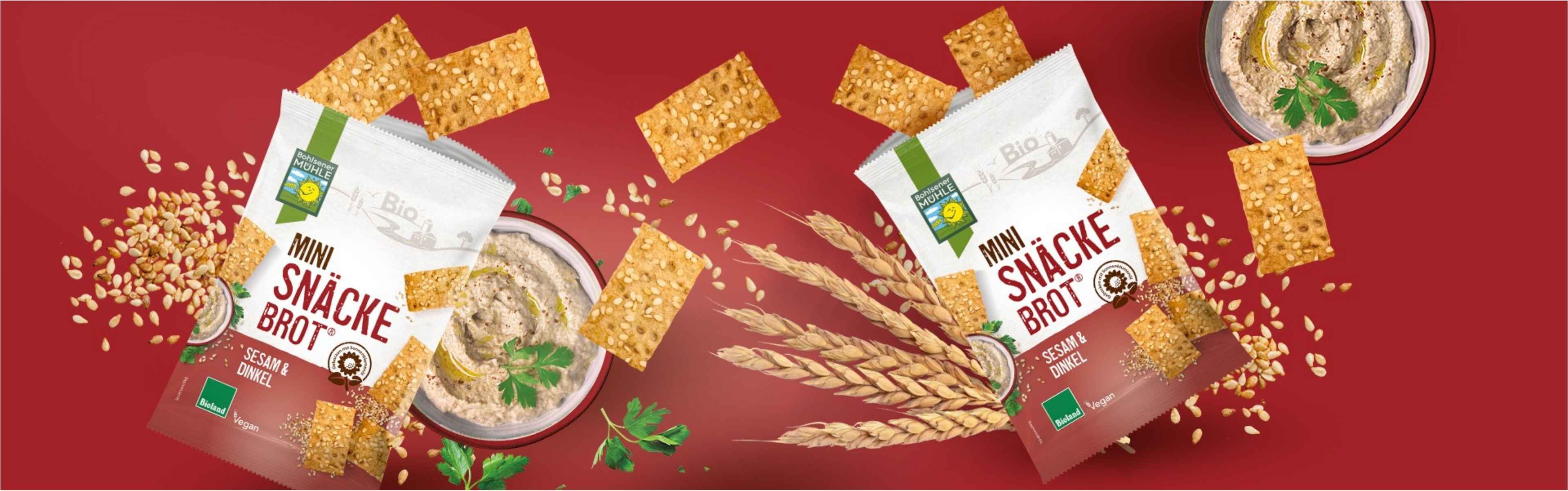 Bohlsener Mühle Mini Snäcke Brot mit Sesam und Dinkel, umgeben von Sesamkörnern und Dip.