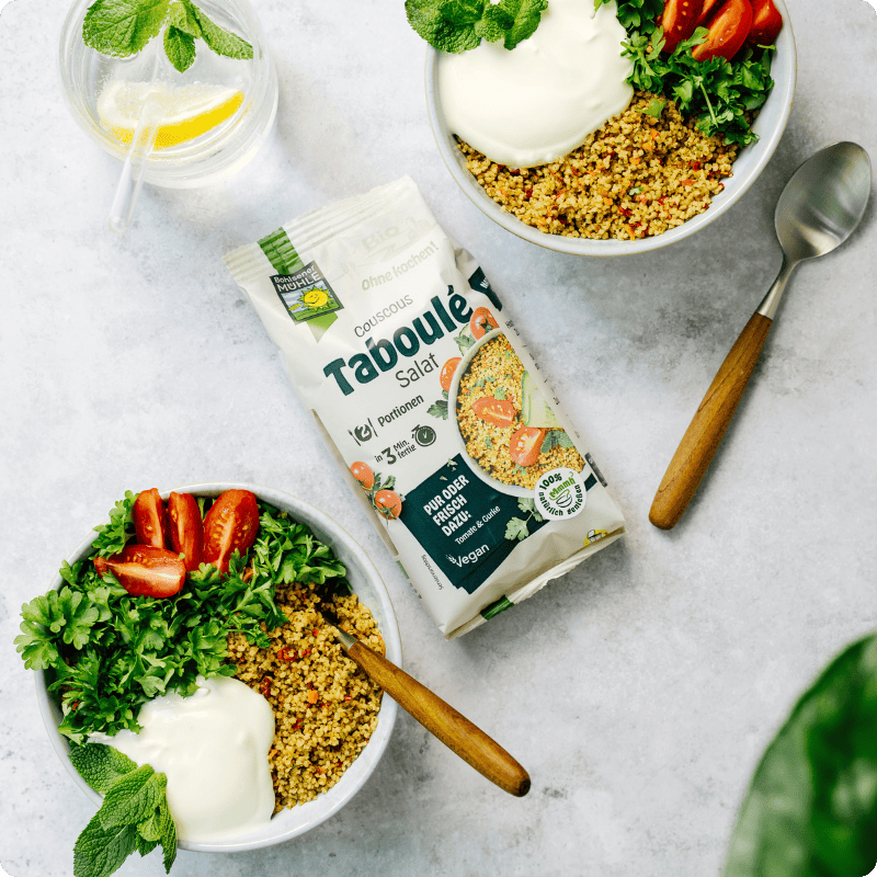 Bohlsener Mühle Couscous Taboulé Salat in Schüsseln mit frischen Tomaten, Kräutern und Joghurt serviert.