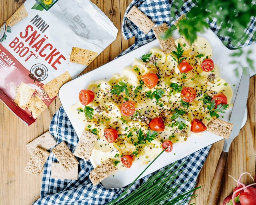 Bohlsener Mühle Bio-Mini-Snäckebrot mit Sesam und Dinkel, serviert mit Butter, Tomaten und Kräutern.