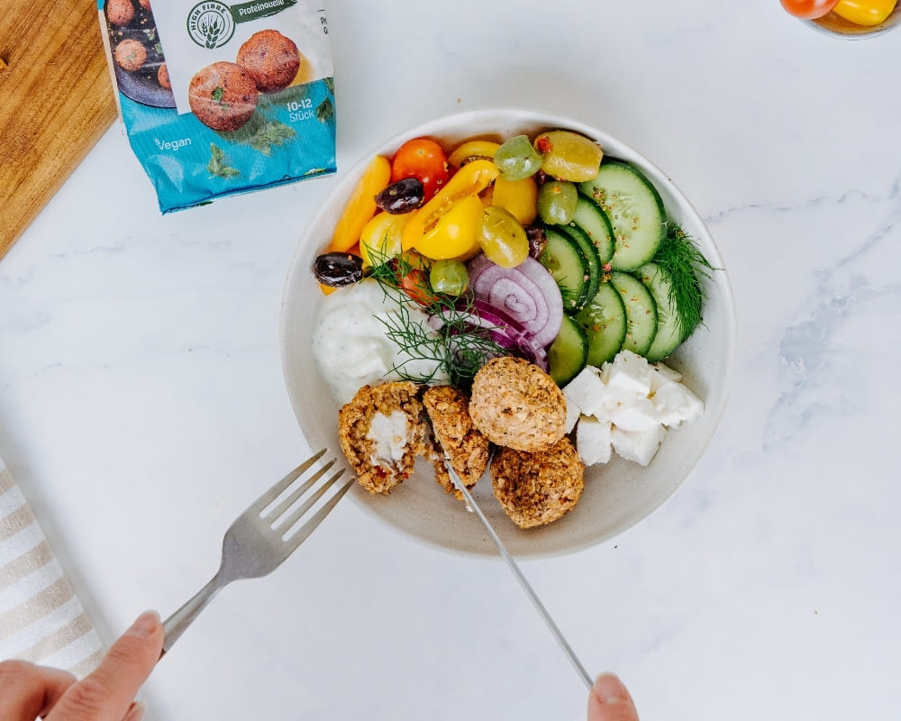 Bohlsener Mühle Falafel-Bällchen in einer Schüssel mit frischem Gemüse, Feta, Oliven und einer hellen Dip-Soße serviert.