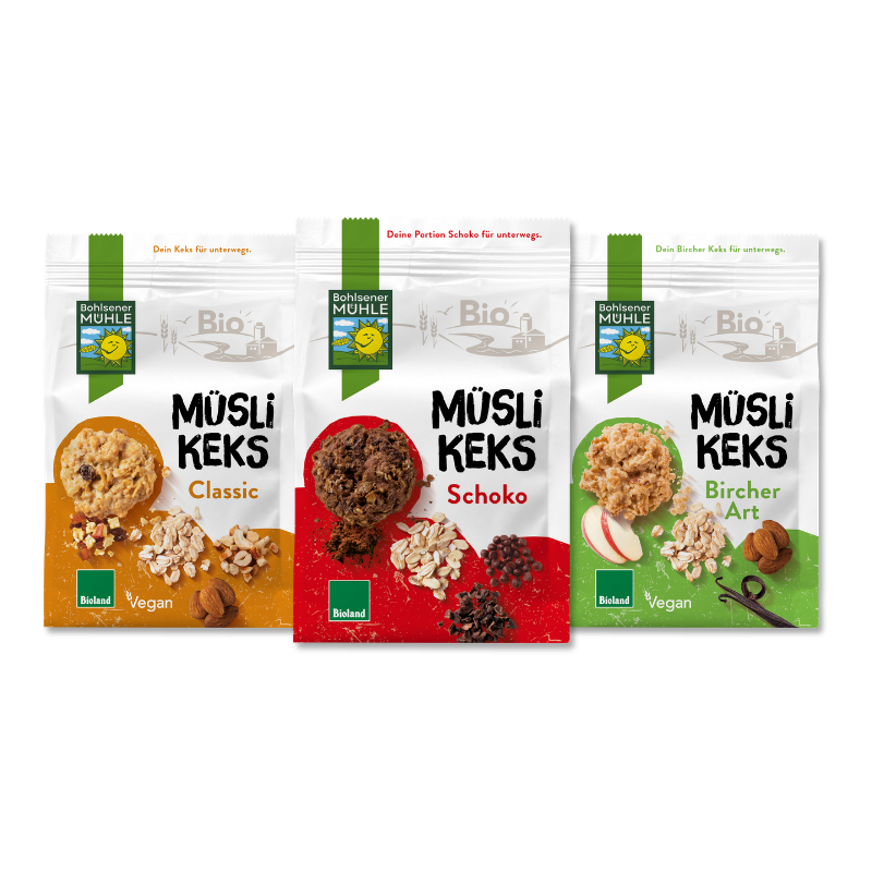 Drei Packungen Bohlsener Mühle Müsli Keks in den Sorten Classic, Schoko und Bircher Art vor schwarzem Hintergrund.