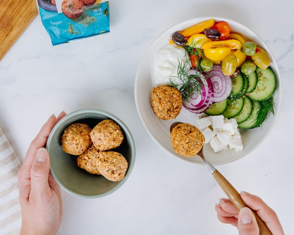 Bohlsener Mühle Falafel-Bällchen in einer Schüssel neben einer Schüssel mit Gemüse, Feta und frischem Dip angerichtet.
