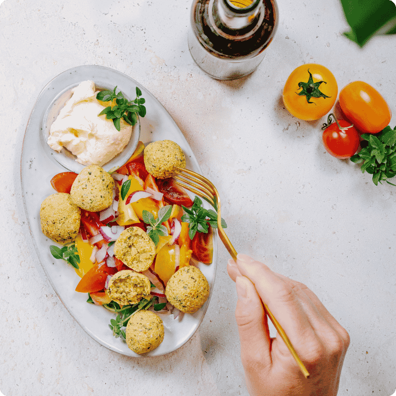 Bohlsener Mühle Falafel Bällchen mit frischem Salat, Dip und Tomaten auf einem Teller serviert.