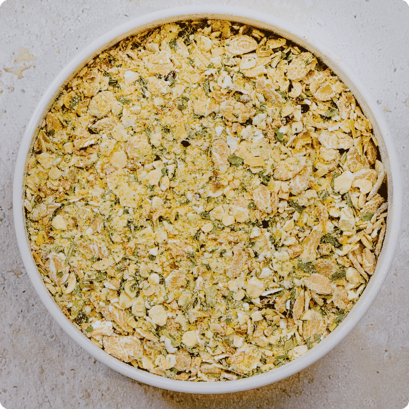 Eine weiße Schale gefüllt mit Bohlsener Mühle Crunchy Haferflocken und grünen Kräutern von oben fotografiert.