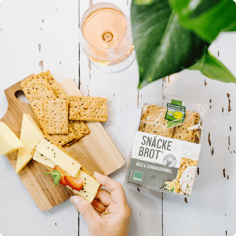 Bohlsener Mühle Snäcke Brot mit Käse und Schwarzkümmel auf einem Holzbrett.