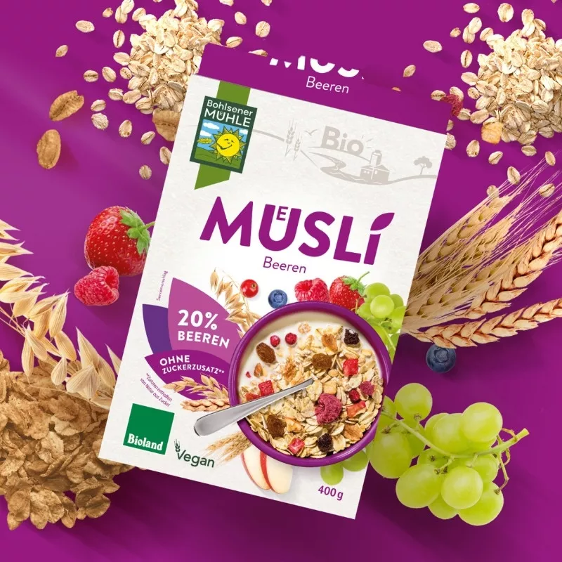 Bohlsener Mühle Müsli mit Bieren, frischen Früchten und Haferflocken auf lila Hintergrund.