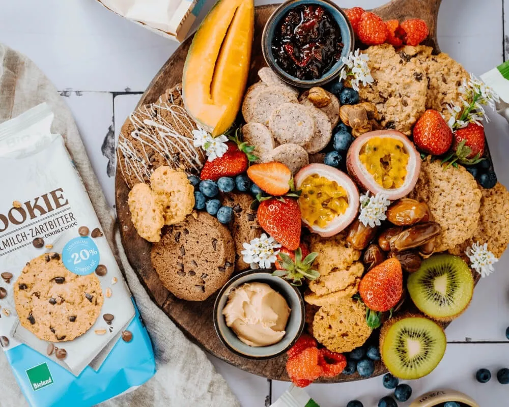 Ein Holzbrett gefüllt mit Bio-Keksen, frischen Früchten, Beeren und Dips.