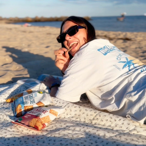 Eine Person genießt Bohlsener Mühle Snacks am Strand, umgeben von Sonnenlicht und Sand.