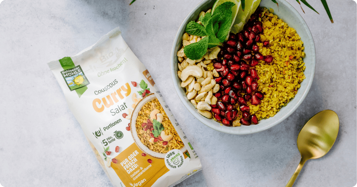 Bohlsener Mühle Couscous Curry Salat in einer Schüssel mit Granatapfel, Cashewkernen und Limette.