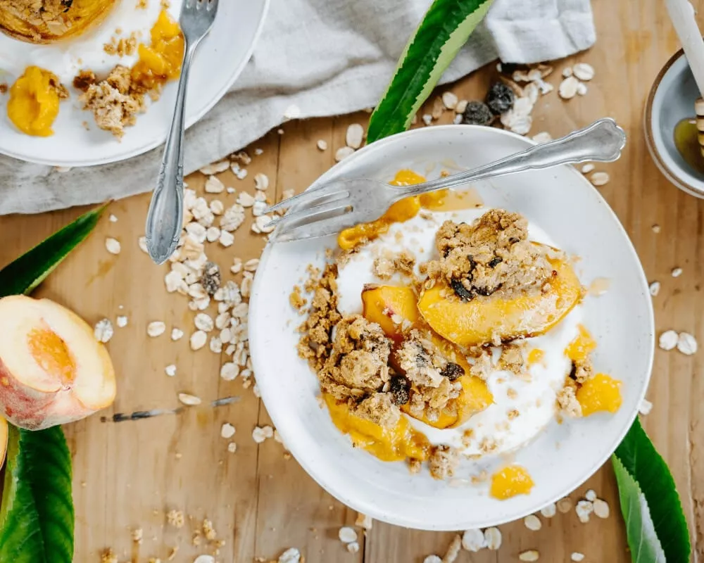 Bio-Pfirsich-Crumble mit Joghurt, Haferflocken und Früchten.