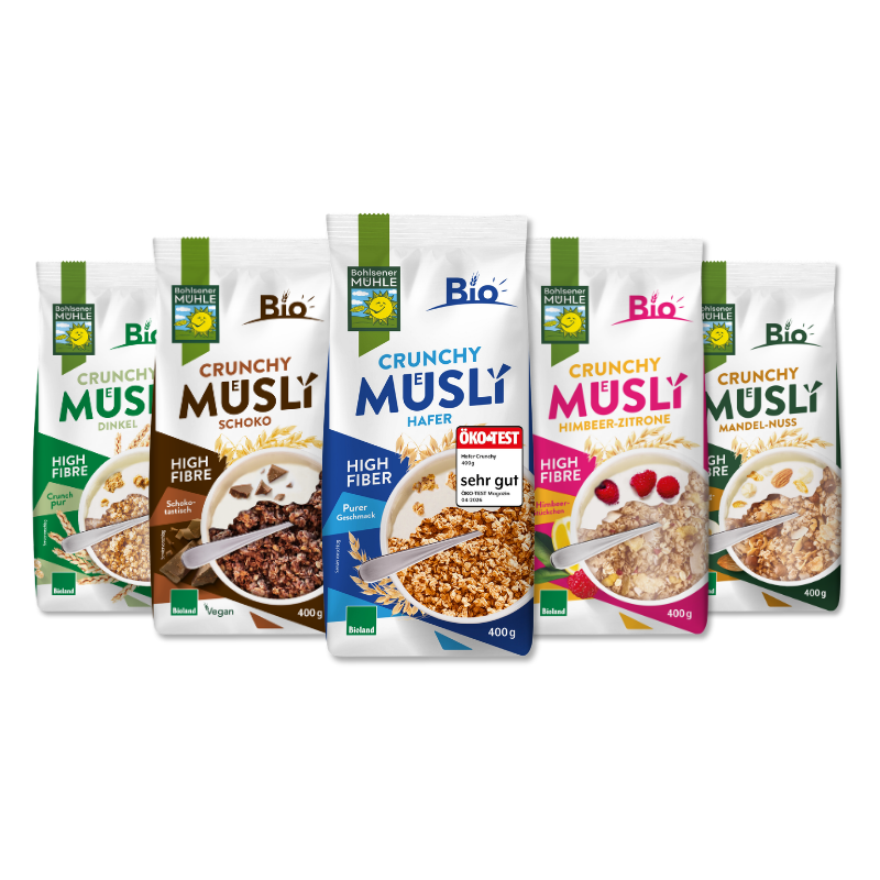 Fünf verschiedene Packungen Bohlsener Mühle Crunchy Müsli in einer Reihe vor schwarzem Hintergrund präsentiert.