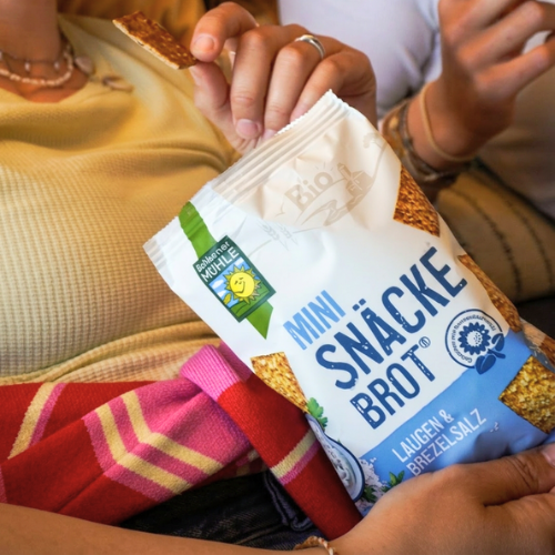 Eine Hand greift nach Bohlsener Mühle Mini Snäcke Brot mit Laugen- und Brezelsalz in einer Tüte.