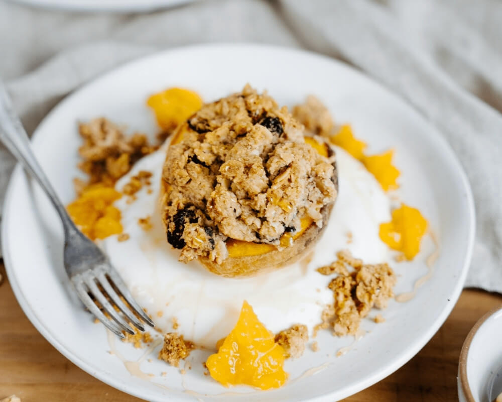 Bio-Gebackener Pfirsich der Bohlsener Mühle mit knusprigem Müsli, Joghurt und Orangenstückchen.