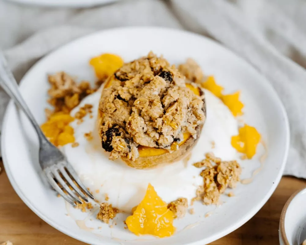 Bio-Gebackener Pfirsich der Bohlsener Mühle mit knusprigem Müsli, Joghurt und Orangenstückchen.