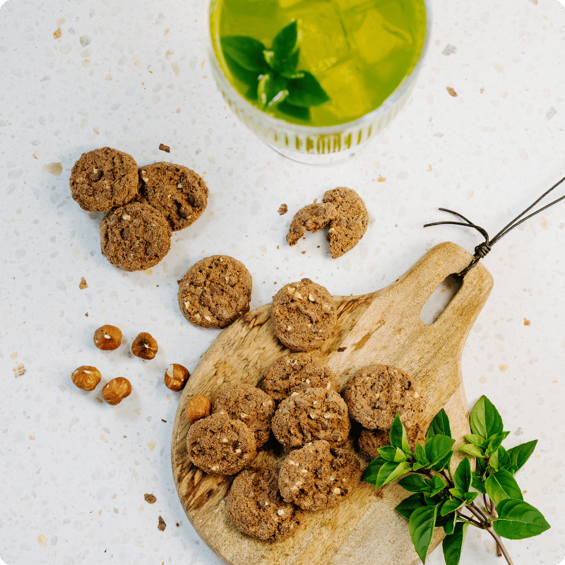 Bohlsener Mühle Crunchy Cookies auf einem Holzbrett mit Nüssen und einem Getränk.
