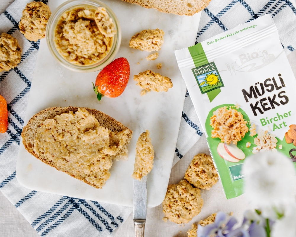 Bohlsener Mühle Müsli Keks Bircher Art auf einem Tisch mit Brot und Erdbeeren.