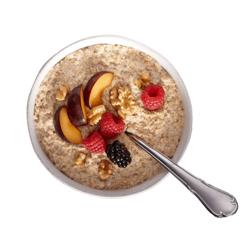 Bohlsener Mühle Porridge mit Pflaumen, Himbeeren, Brombeeren und Walnüssen in einer Schale mit einem Löffel serviert.
