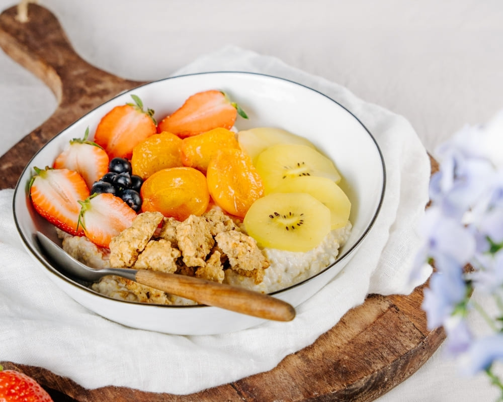 Schüssel mit Bohlsener Mühle Knusprige, frische Früchte und Haferbrei auf einem Holzbrett.