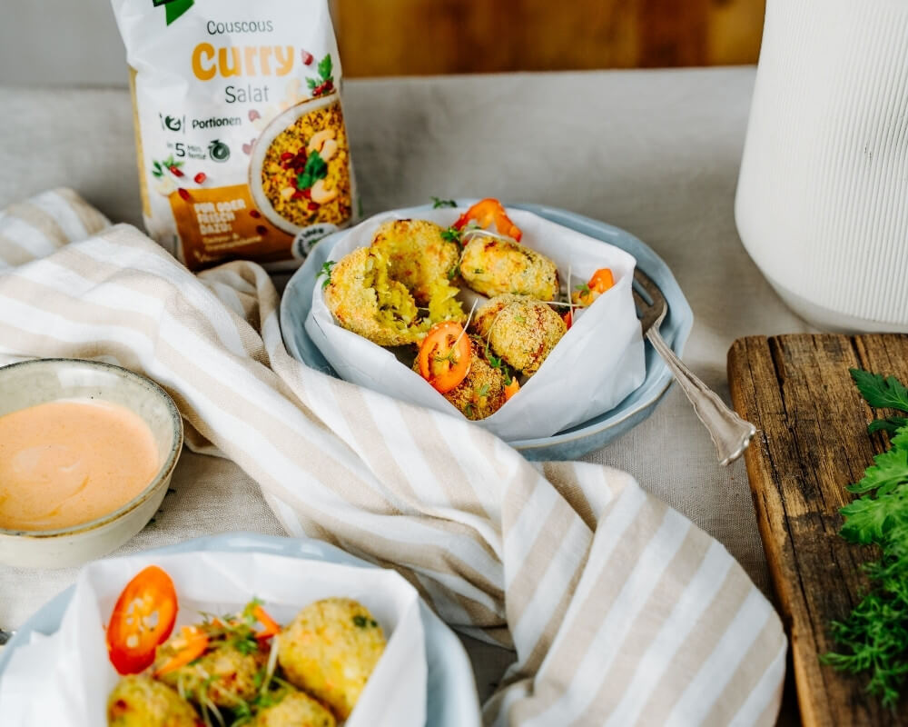 Bio-Curry-Couscous-Salat der Bohlsener Mühle, knusprige Snacks und Dip-Sauce auf einem Tisch.