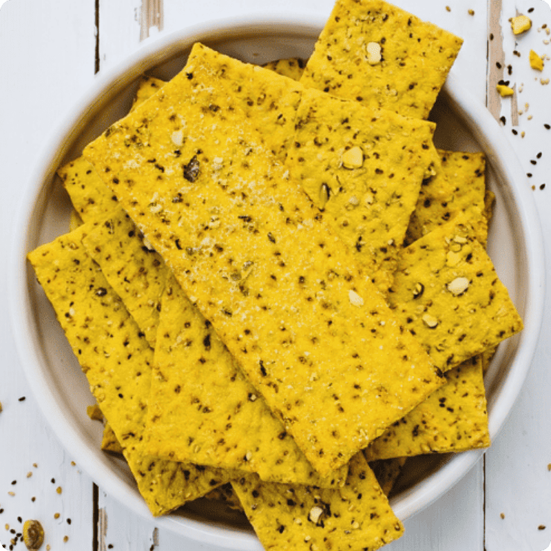 Gelbe Bohlsener Mühle Crunchy Cracker mit Saaten in einer weißen Schale auf einem hellen Holztisch angerichtet.