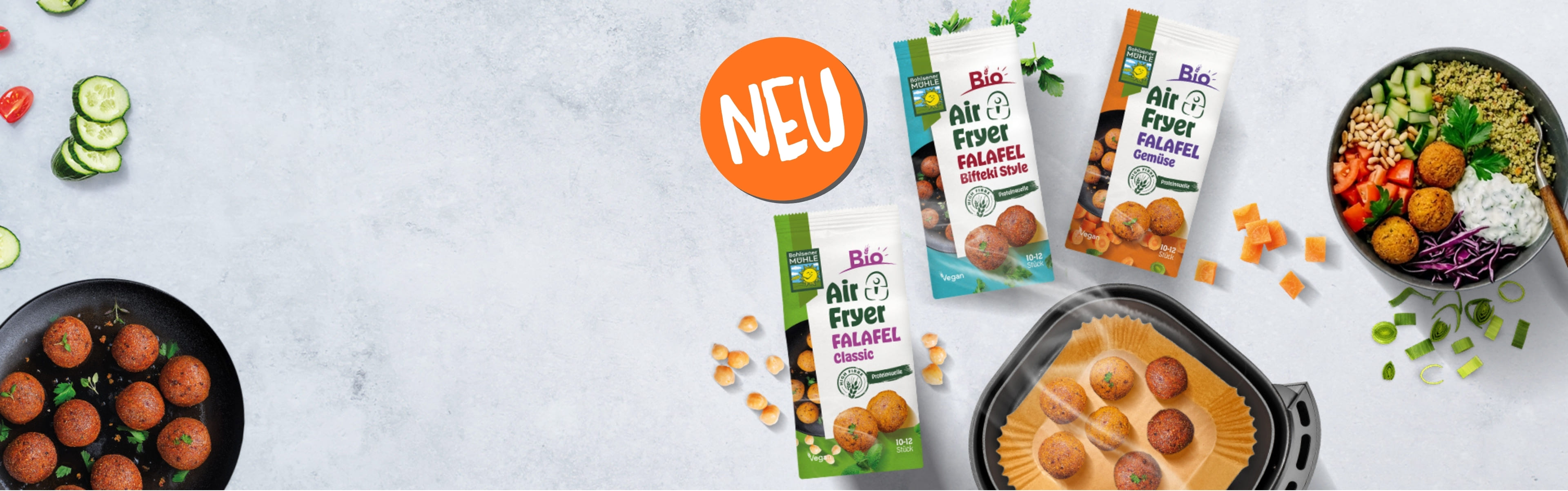 Bohlsener Mühle Air Fryer Falafel Packungen neben einer Heißluftfritteuse und einer Schüssel mit frischem Gemüse.