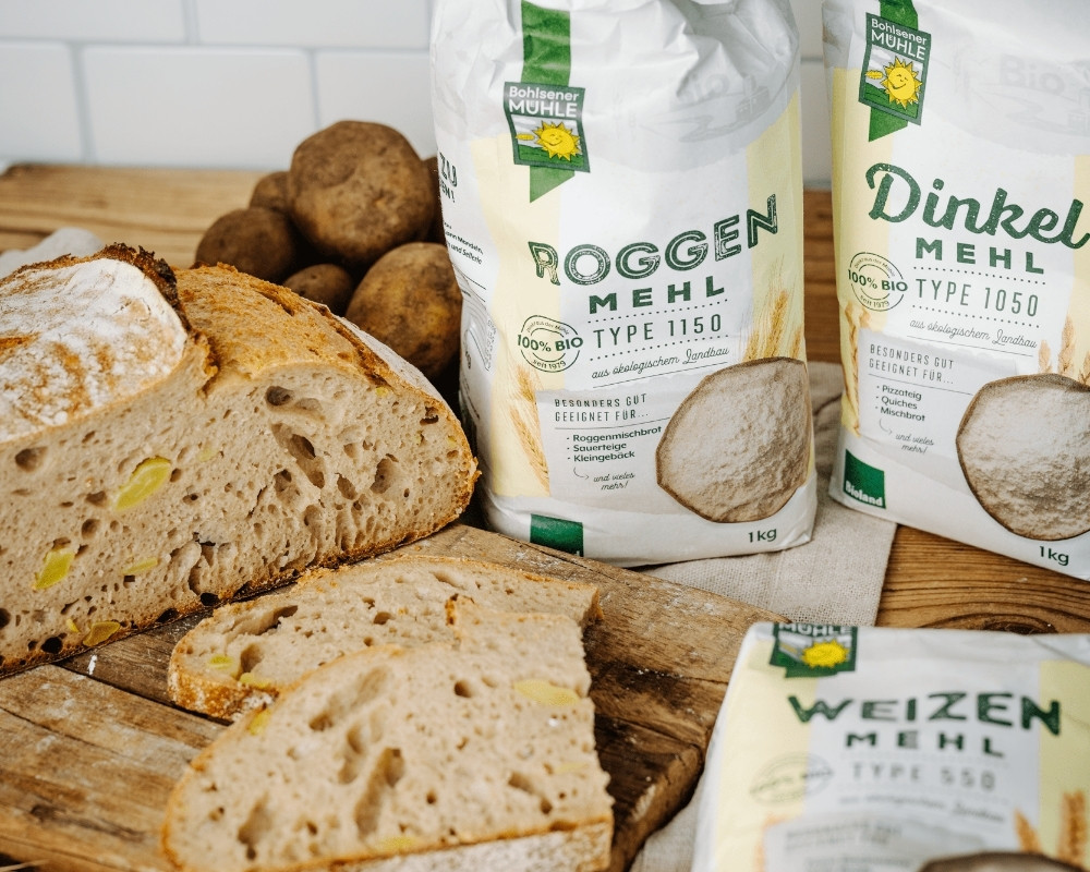 Bohlsener Mühle Roggenmehl, Dinkelmehl und Weizenmehl neben frischem Brot und Kartoffeln.
