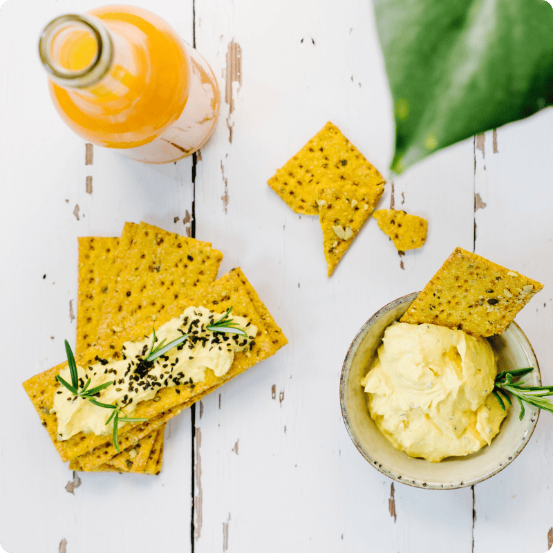 Bohlsener Mühle Crunchy Cracker mit gelbem Dip und Rosmarin auf einem weißen Holztisch serviert.