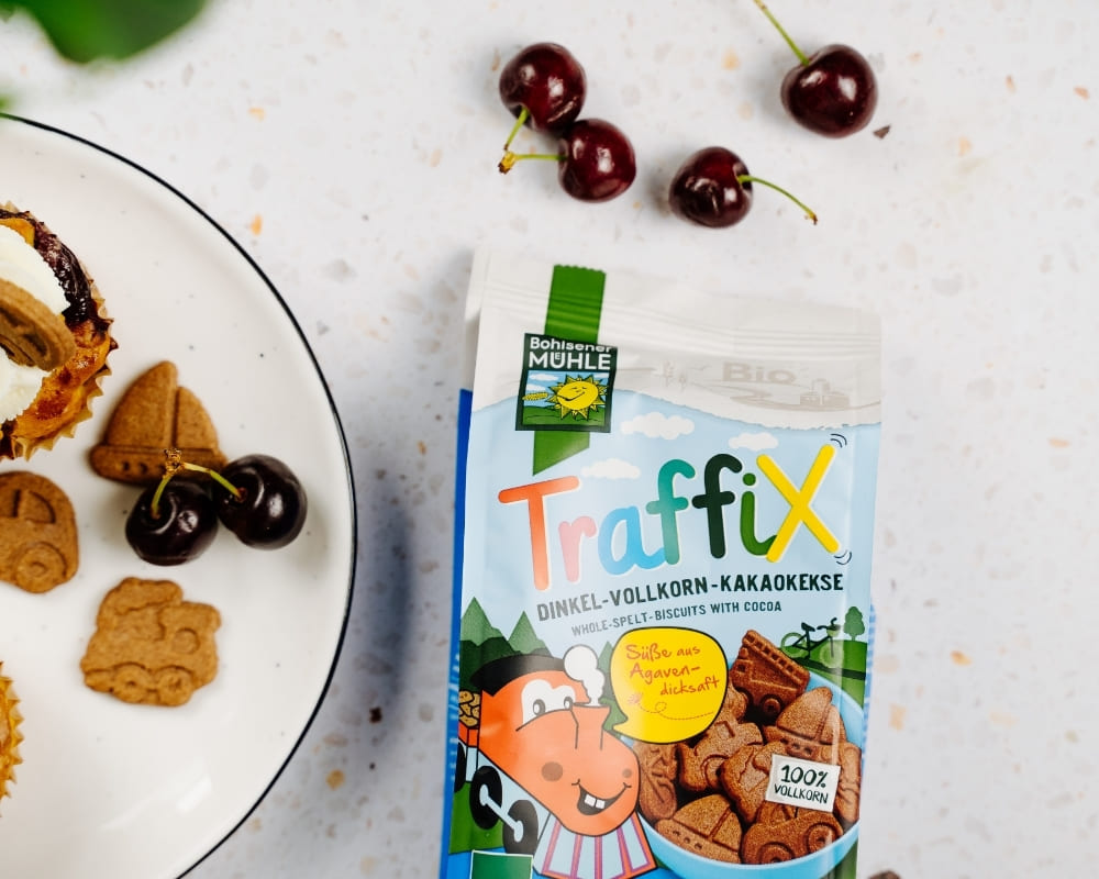 Bohlsener Mühle Traffix Dinkel-Vollkorn-Kakaokekse neben einem Teller mit Keksen und frischen Kirschen.
