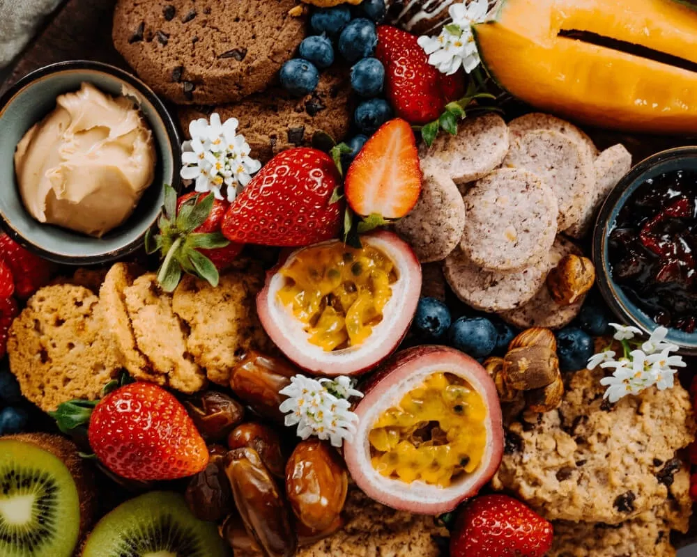 Eine lebendige Platte mit Bio-Snacks der Bohlsener Mühle, darunter Kekse, Cracker, frische Beeren, Passionsfrucht und Kiwi.