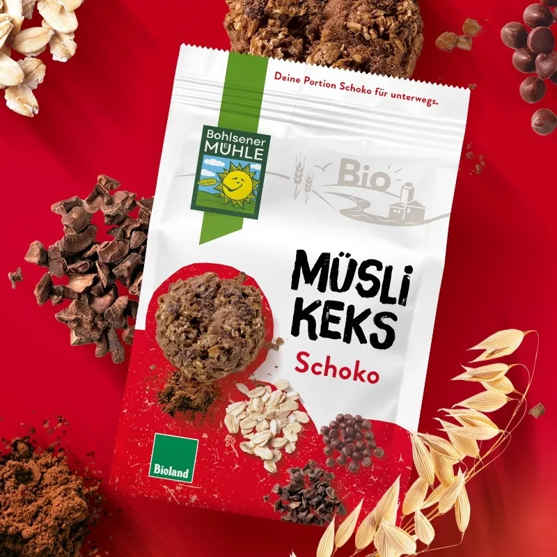 Bohlsener Mühle Müsli Keks Schoko auf rotem Hintergrund mit Schokoladenstückchen und Haferflocken.