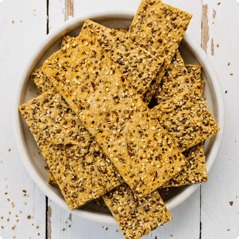Bohlsener Mühle Crunchy Cookie Knäckebrot mit vielen Körnern in einer weißen Schale auf einem Holztisch.