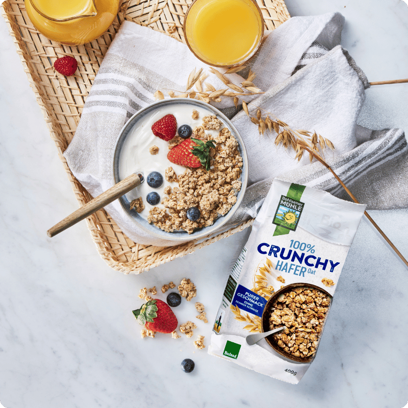 Bohlsener Mühle 100% Crunchy Hafer mit Joghurt, Beeren und Saft auf einer Tablette.